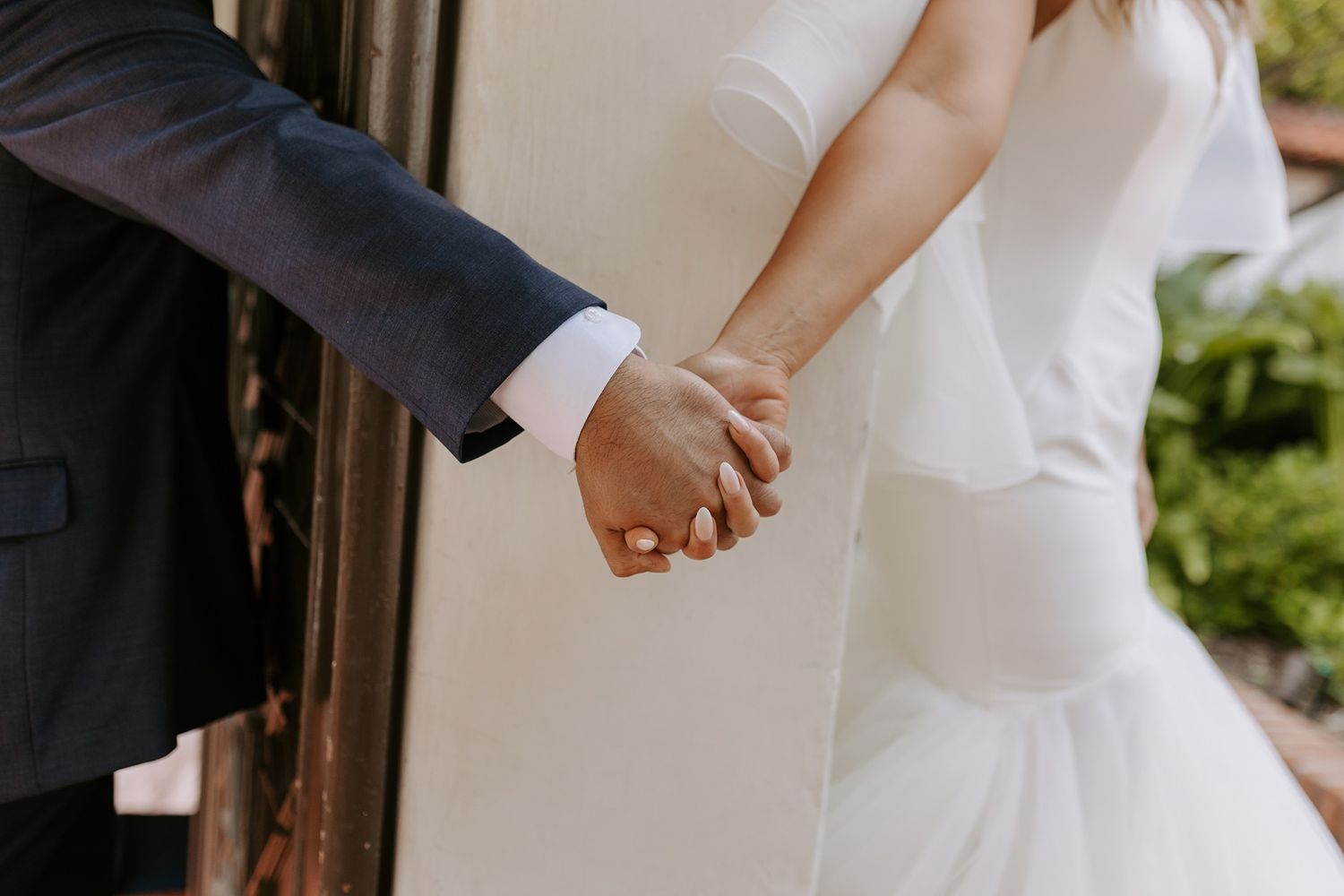 Bride and groom holding hands in wedding attire, showcasing a white bridal gown and navy suit.