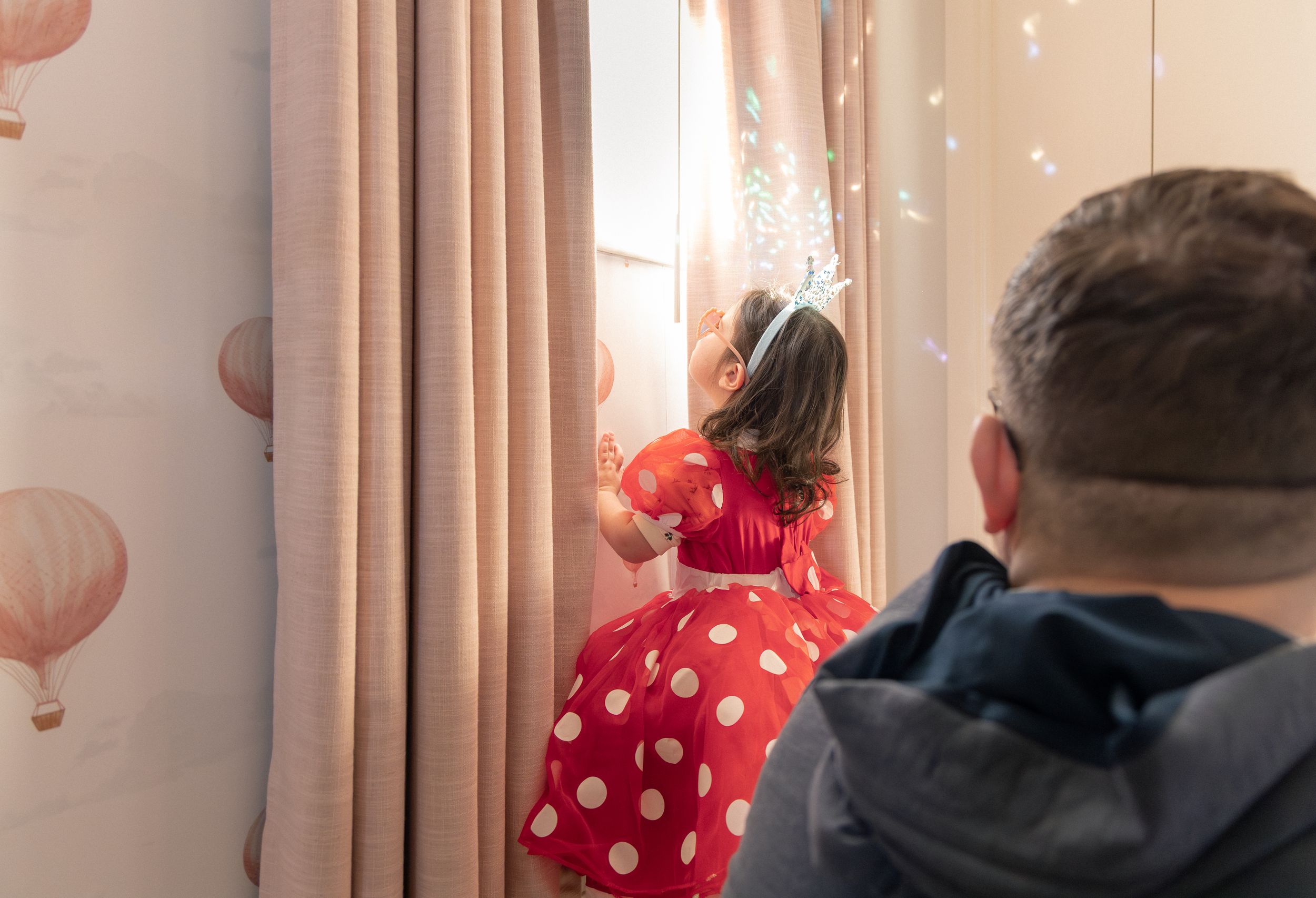 A parent and child sit together in a cozy living room with pink balloons creating a festive atmosphere.