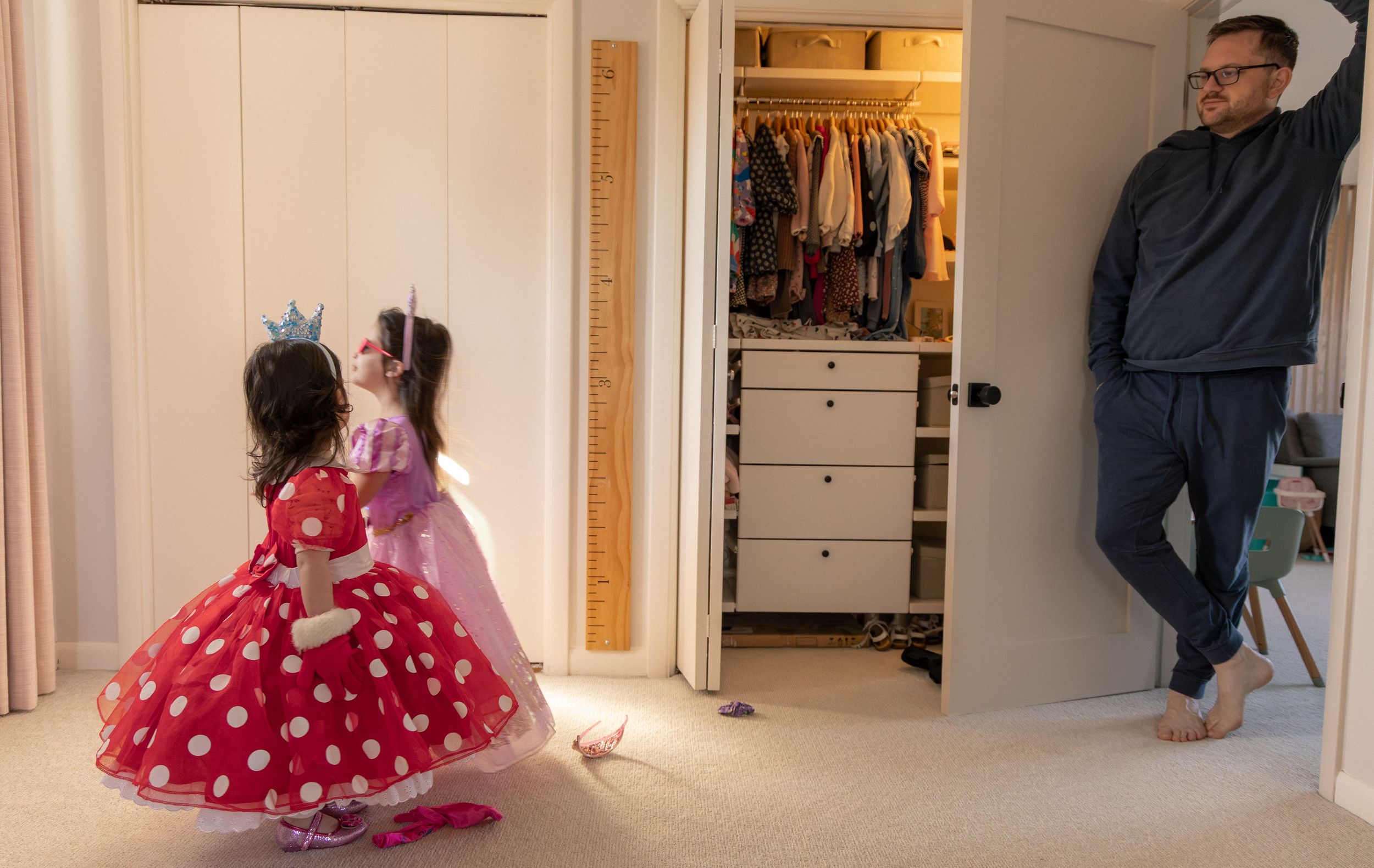 A child in a red polka dot dress twirls and dances in a bright hallway with wooden floors.