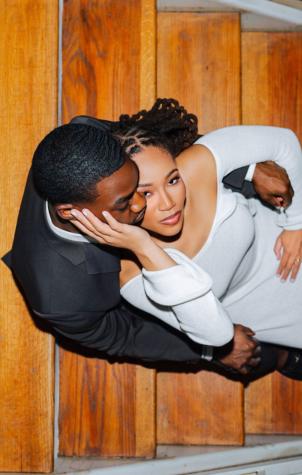 Romantic couple sharing a tender kiss, captured from above on wooden stairs in formal wear.