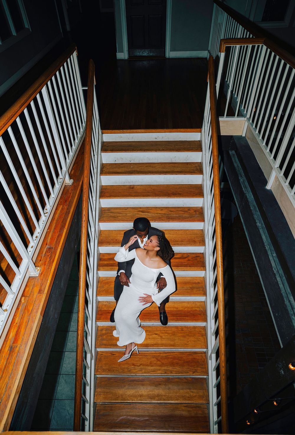 Aerial view of couple embracing on wooden staircase, woman in white dress and man in dark suit.