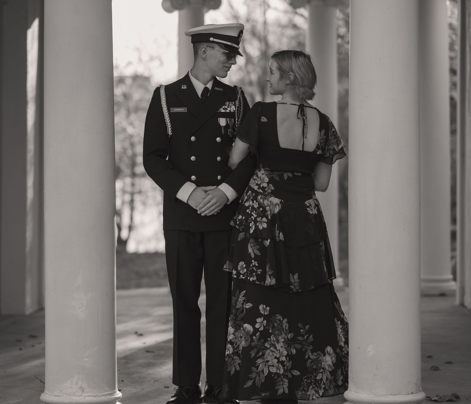 Black and white photo of a military couple in formal attire standing between white columns.