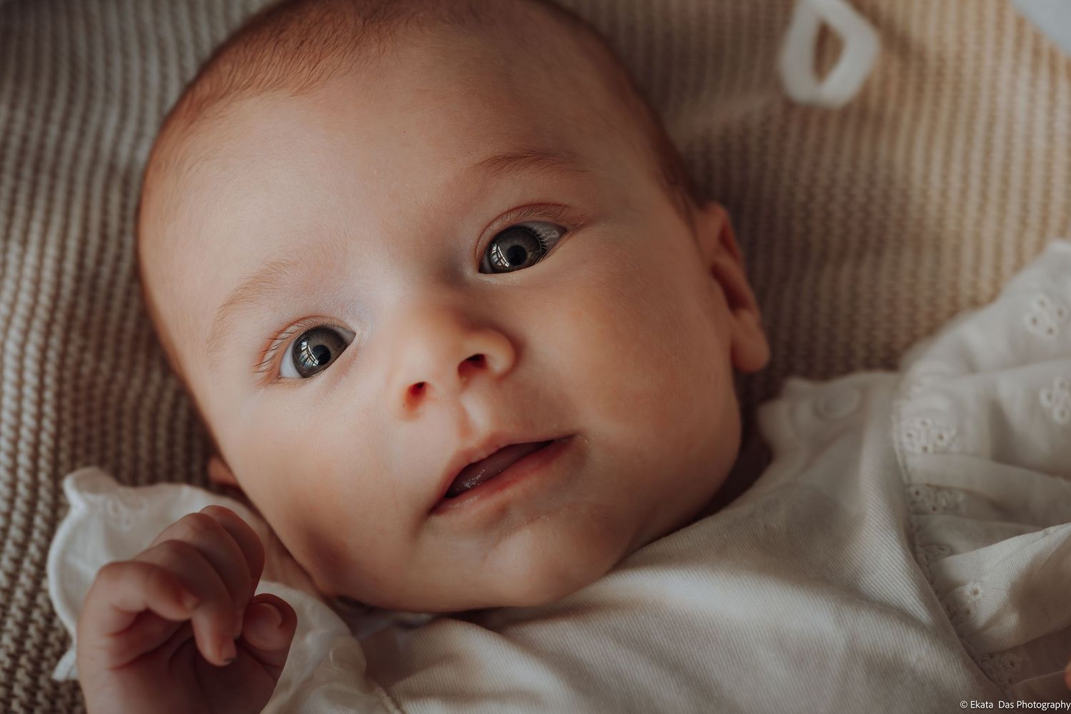 Close-up portrait of a newborn baby with big eyes lying on a soft blanket in natural light.