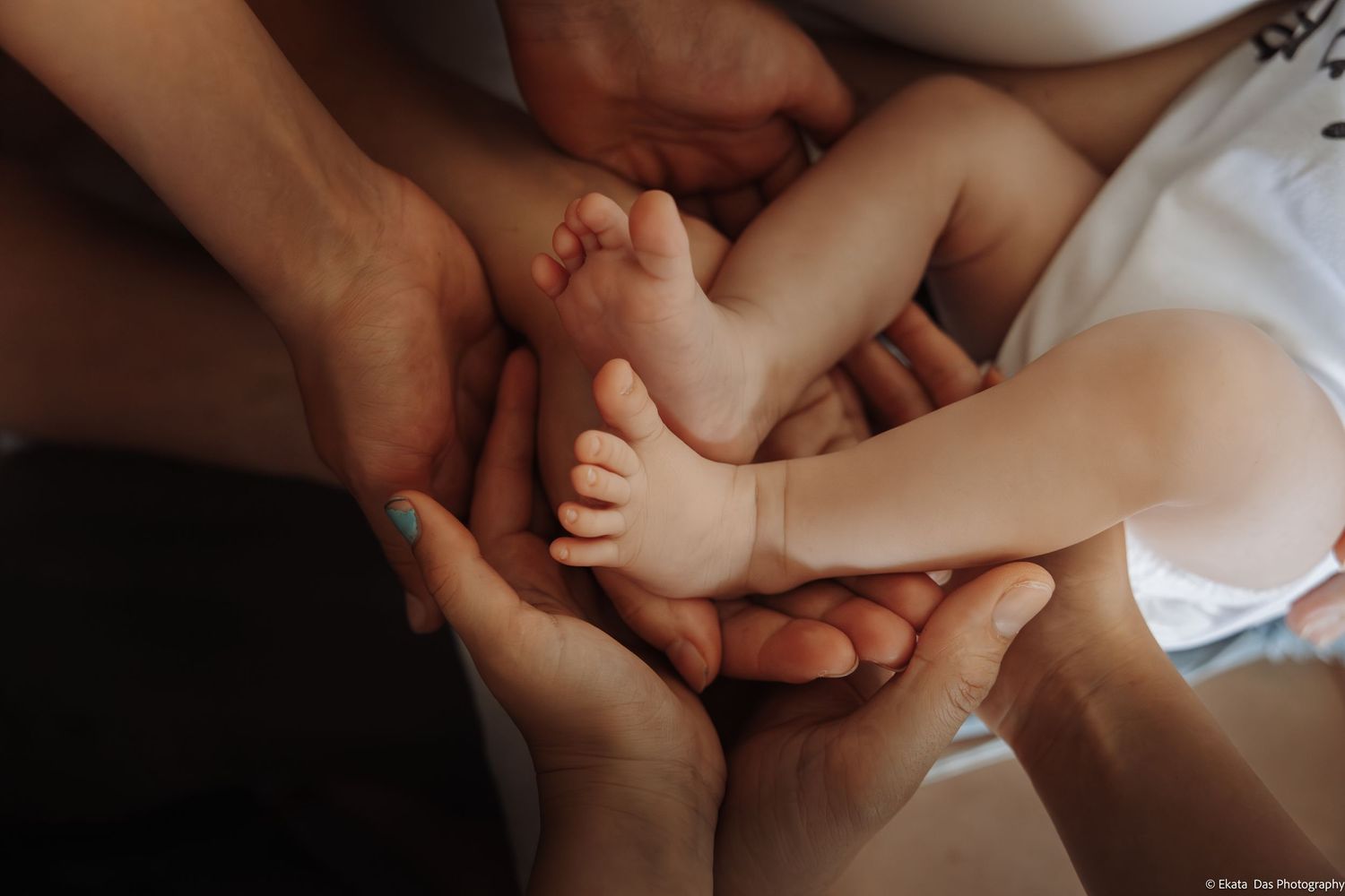Multiple hands cradling tiny newborn baby feet, a heartwarming family bonding moment captured in soft natural light.