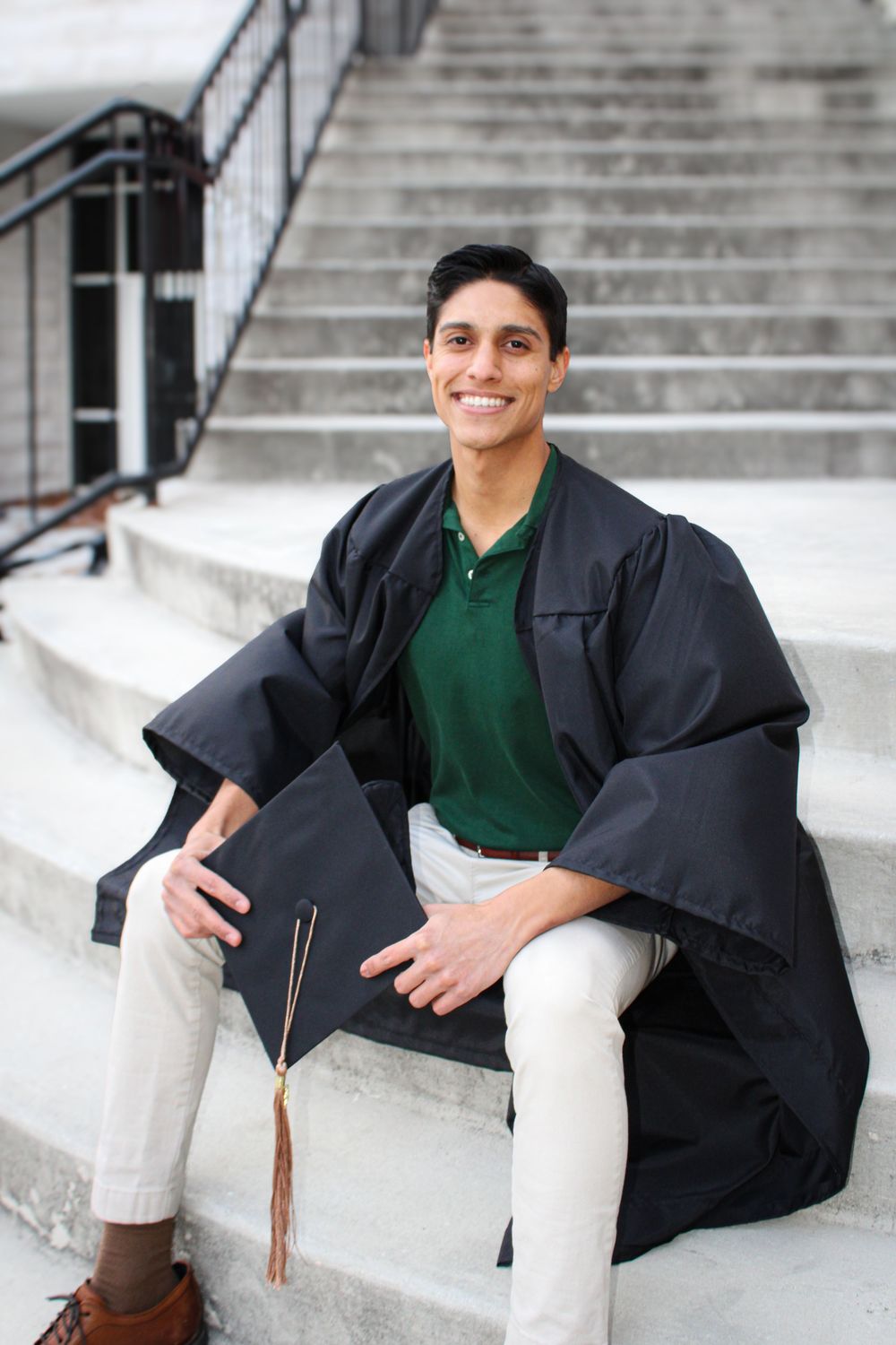 man sitting on stairs holding graduation cap