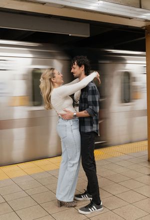Couple embracing romantically on a subway platform as a train passes by in motion blur behind them.