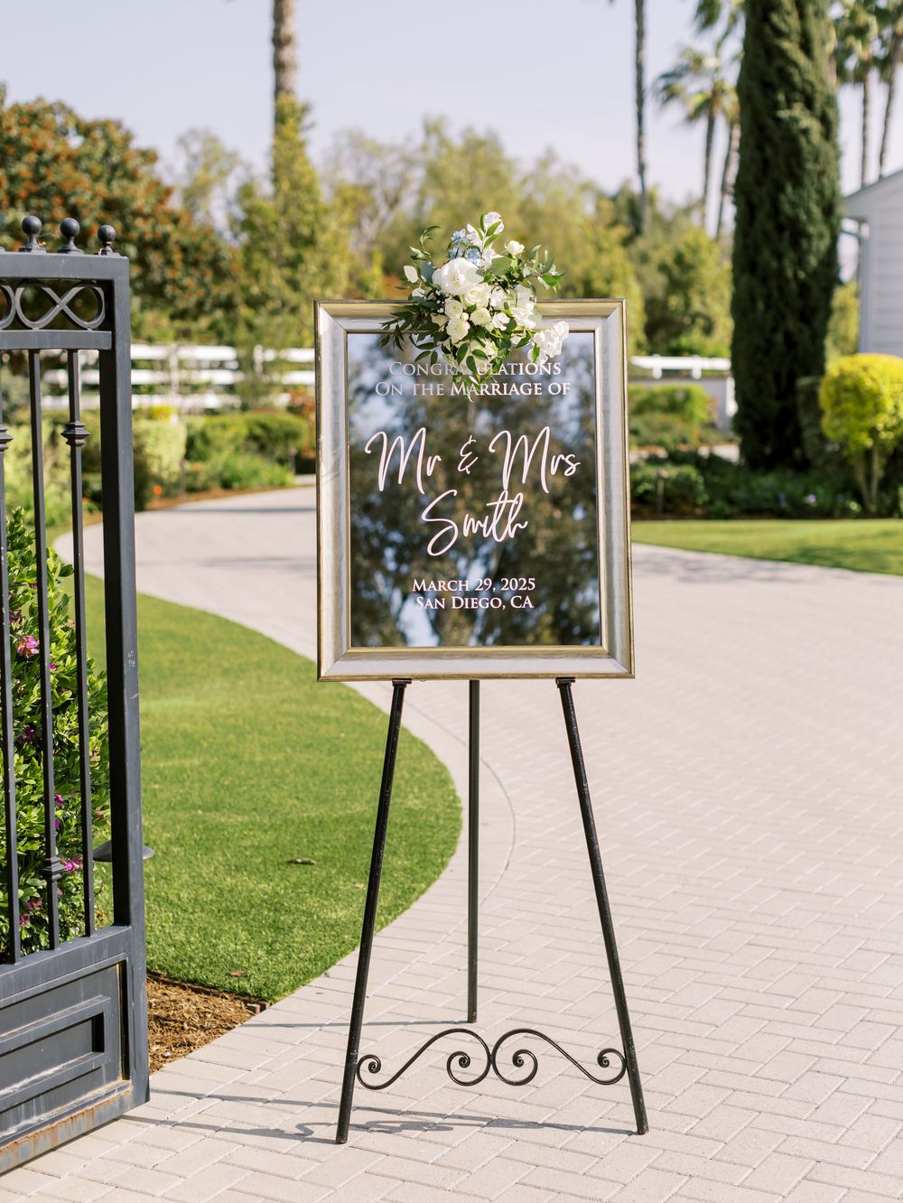 Wedding signage displayed on black easels along a curved pathway with palm trees in the background.