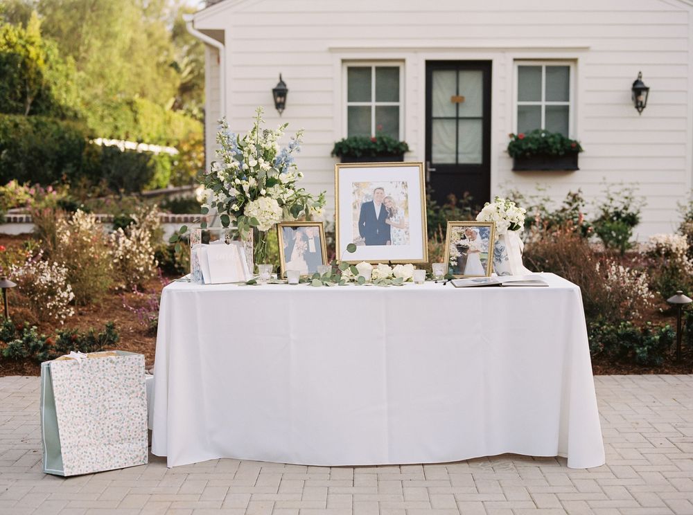 Long white tablecloth-covered tables with place settings arranged on an outdoor patio for an elegant event.