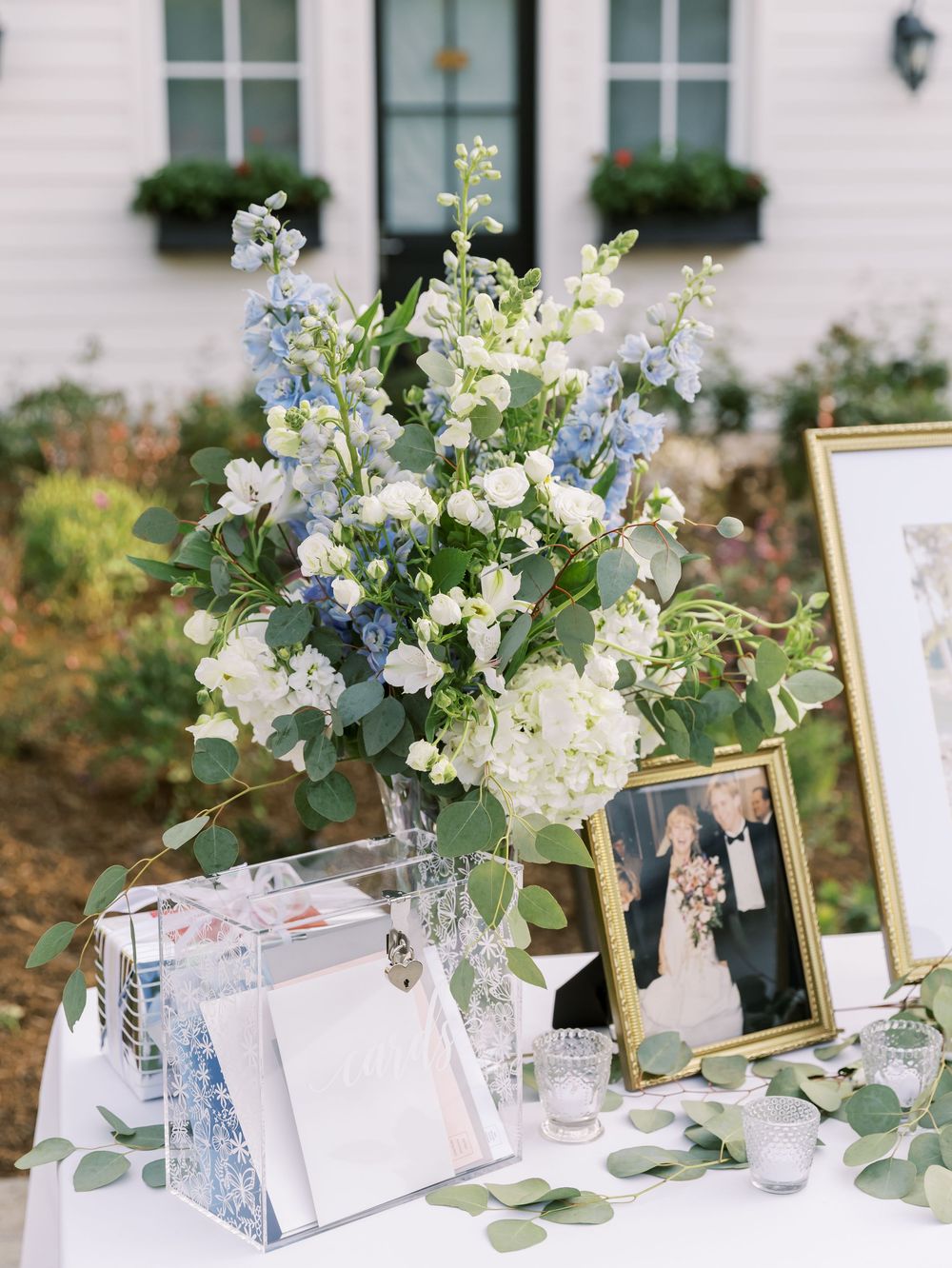 Elegant wedding reception table with white floral centerpieces, gold frames, and delicate greenery arrangements.
