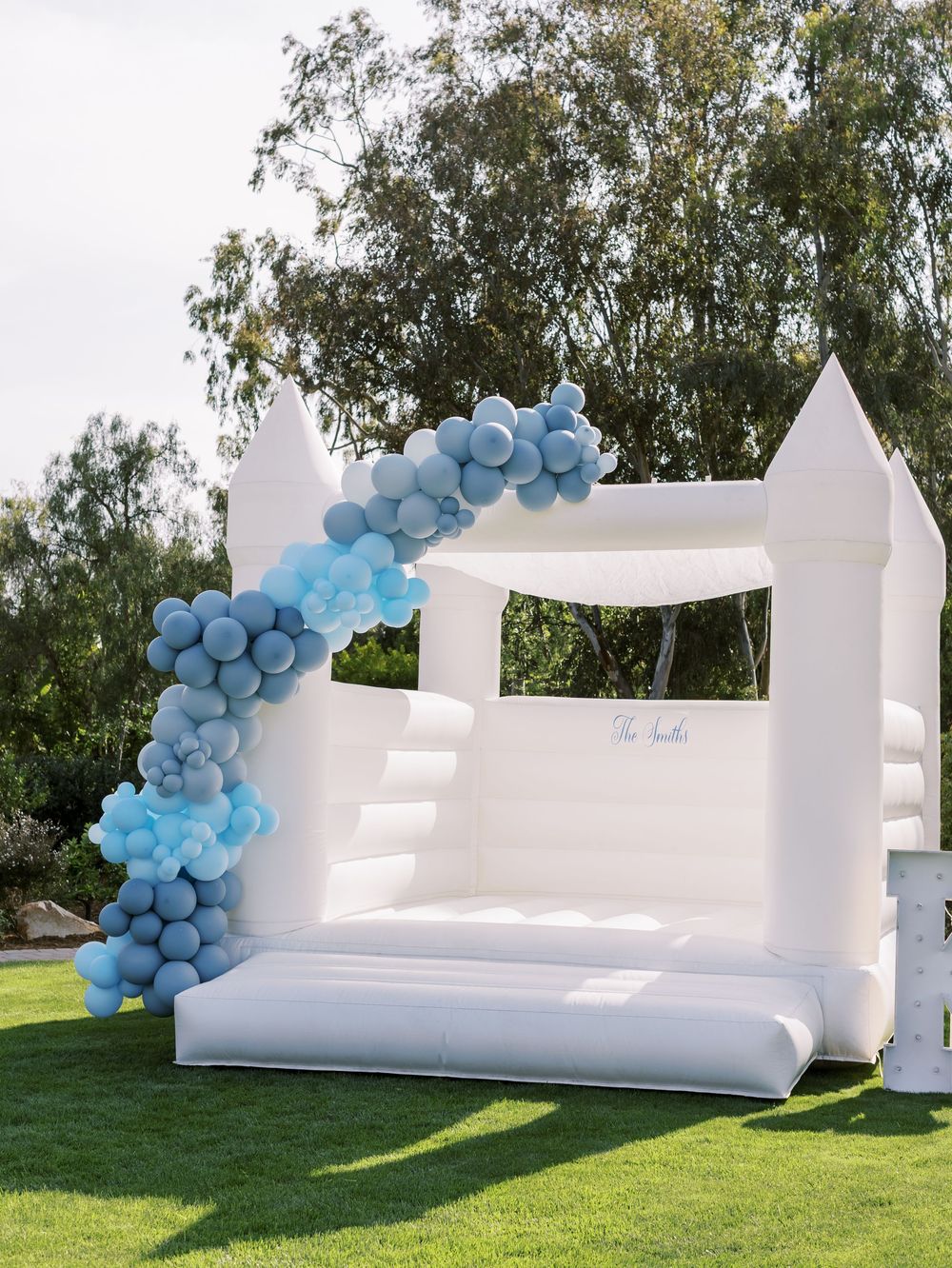 White inflatable bounce house decorated with blue balloon garland for an outdoor event.