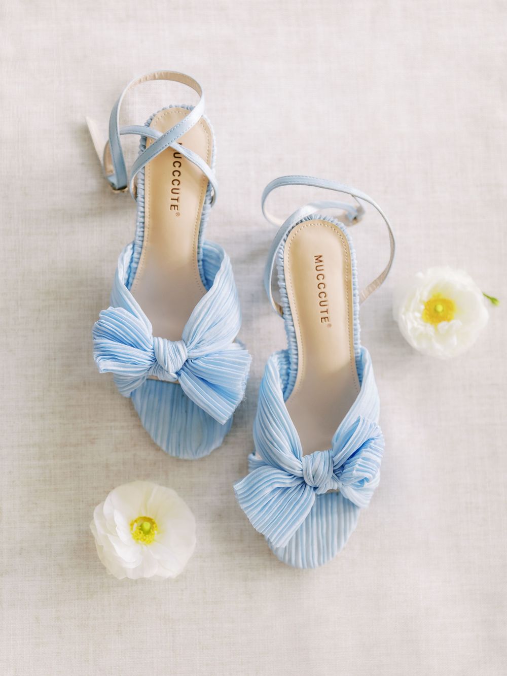Light blue bow-adorned wedding shoes with delicate white flowers on a neutral background.
