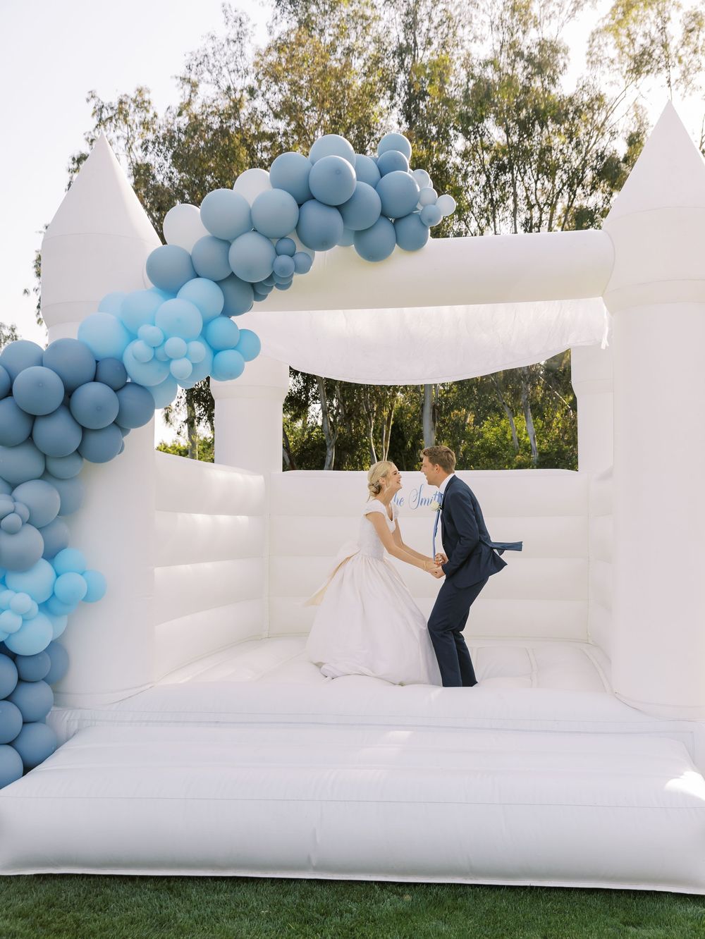 White bounce house with blue balloon arch decorations at an outdoor event.
