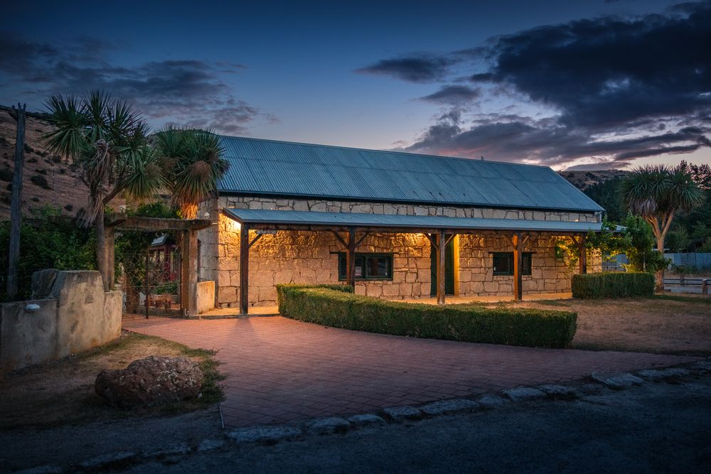 Rustic stone pavilion lit up at twilight with palm trees and landscaping.