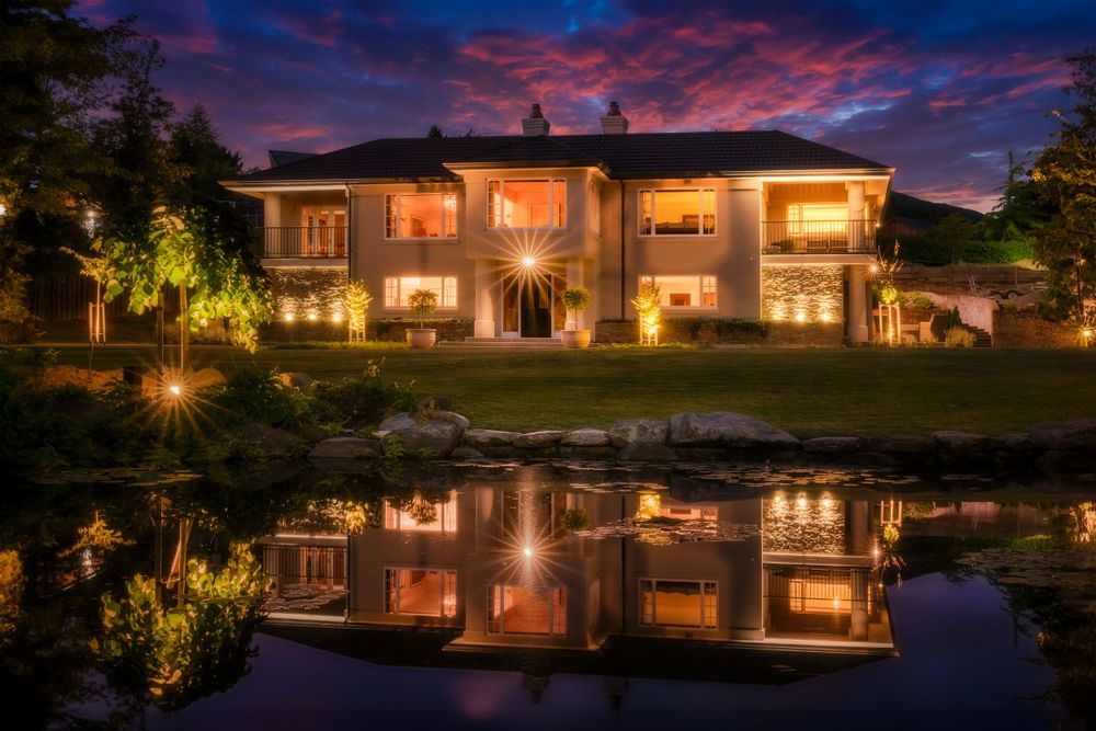 Elegant mansion with perfect reflection in pond under vibrant sunset sky.