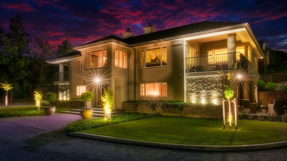 Modern luxury home with balcony and landscape lighting at dusk.