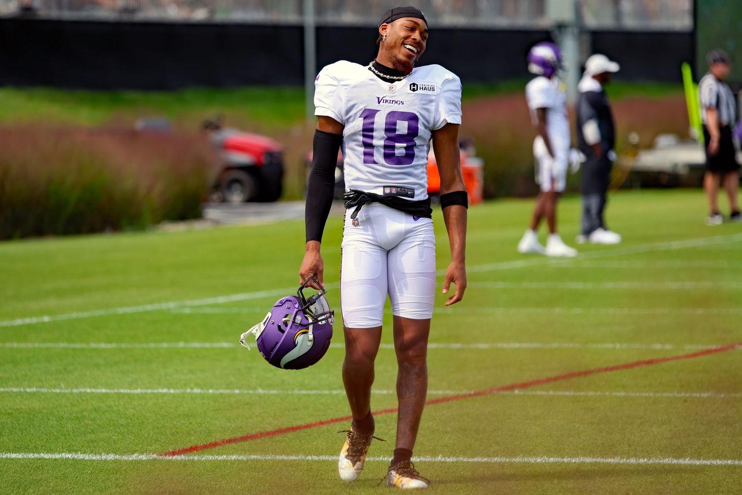 Football player (Justin Jefferson) in white uniform with number 18 holds purple helmet on practice field during training session.