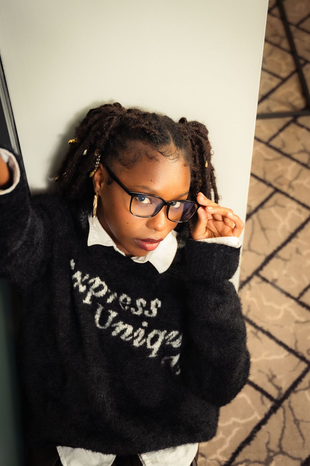 Artistic angle shot showing black sweater with text and glasses against neutral background.
