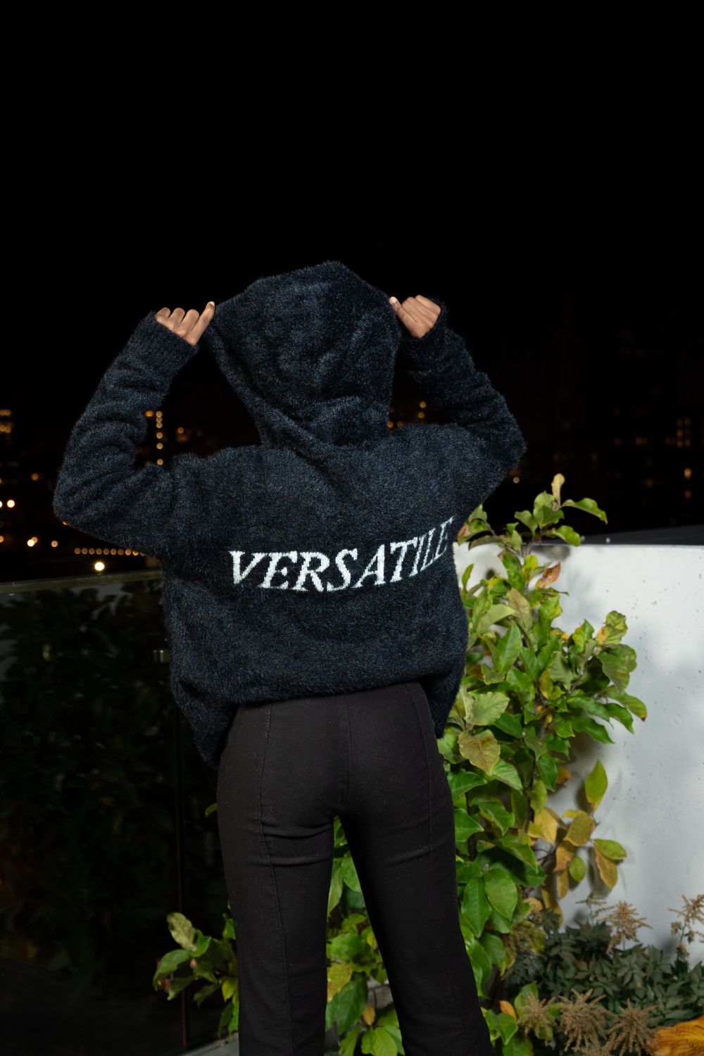 Back view of person wearing black hoodie with 'VERSATILE' text at night.