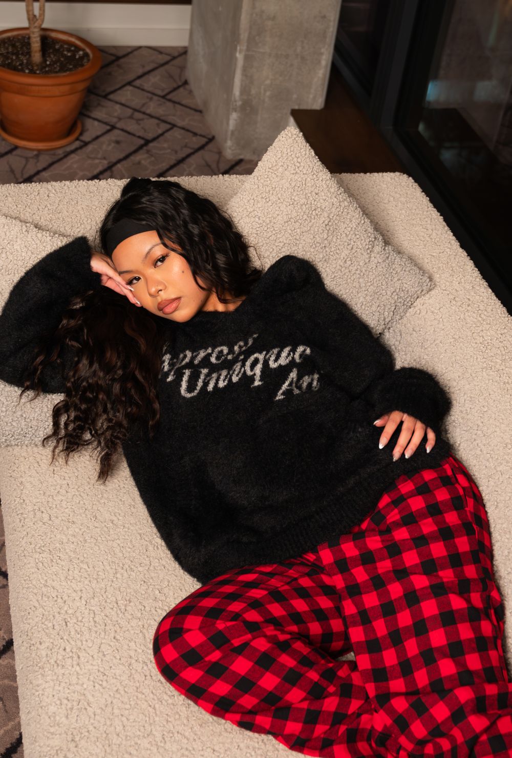 Cozy indoor portrait featuring black sweater and red plaid pajama pants on white couch.