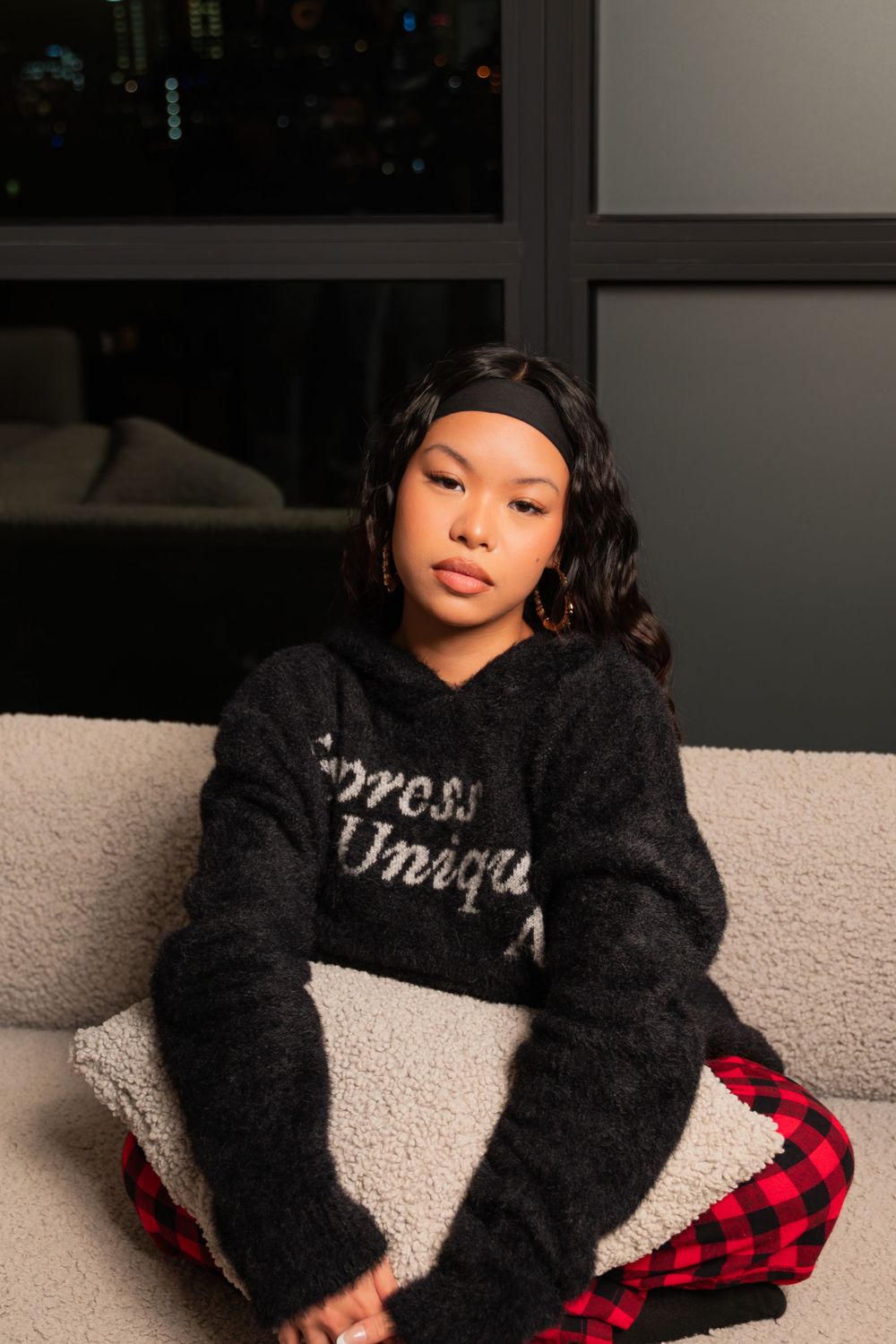 Lifestyle portrait on couch wearing fuzzy black sweater and red buffalo plaid pants.