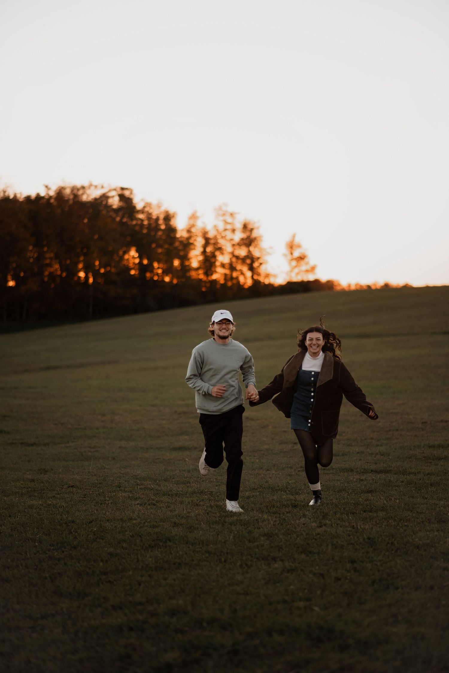 Couple playfully running through open field at sunset in Buffalo, NY