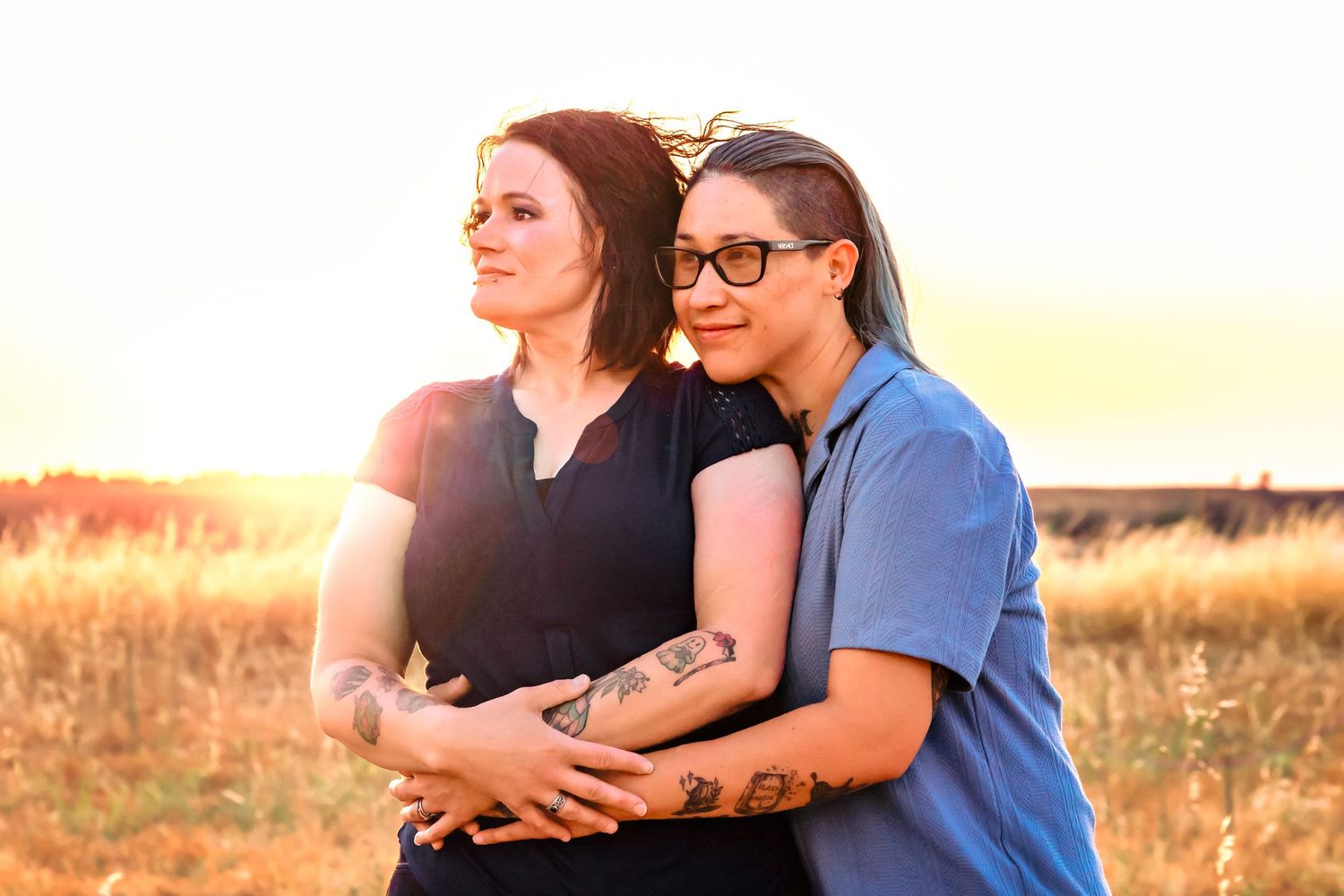 LGBQ couple stare off into distance as they embrace with beautiful golden sun in background in Fresno,ca