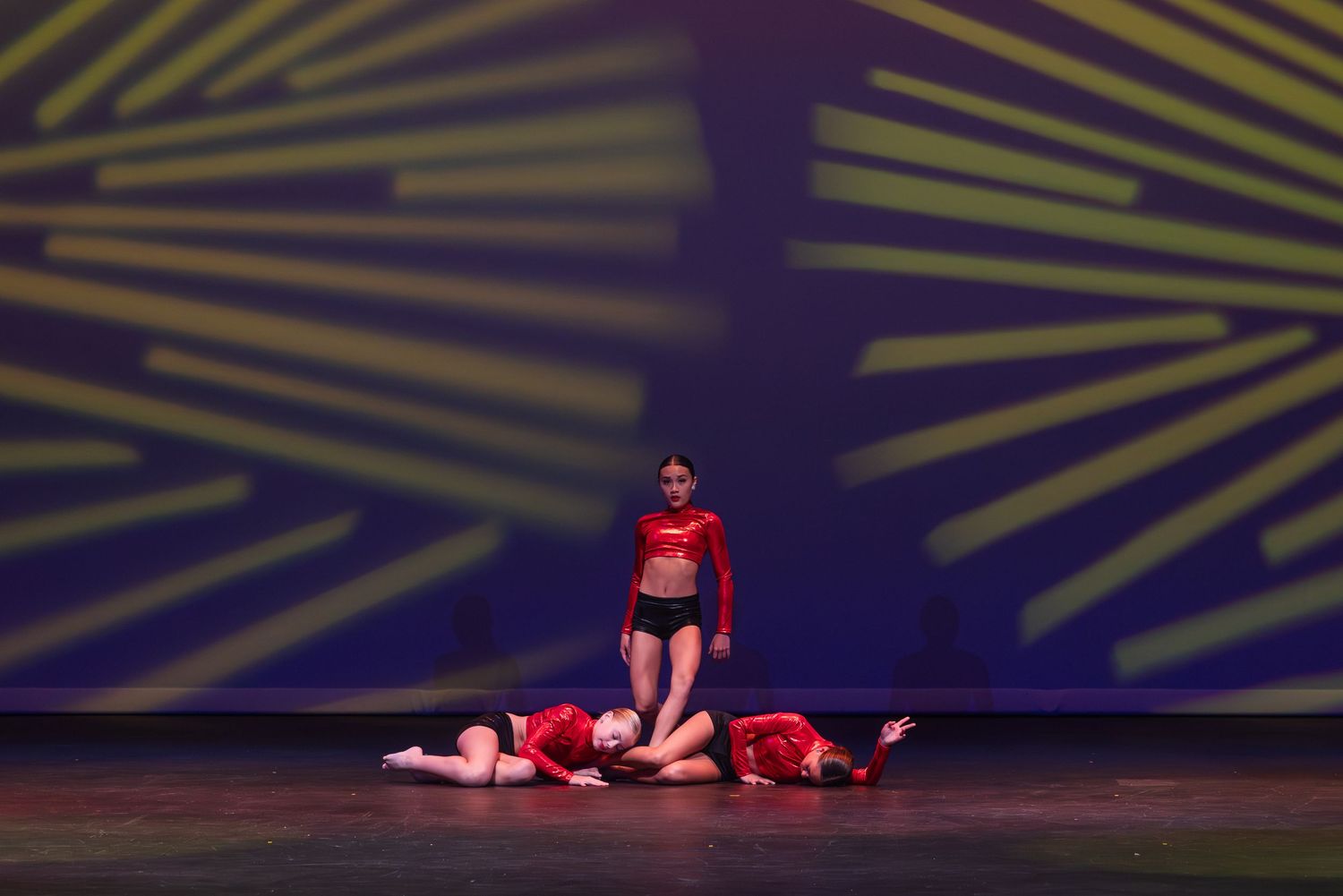 Dancers in red costumes perform on dark stage with dramatic yellow lighting effects in background.