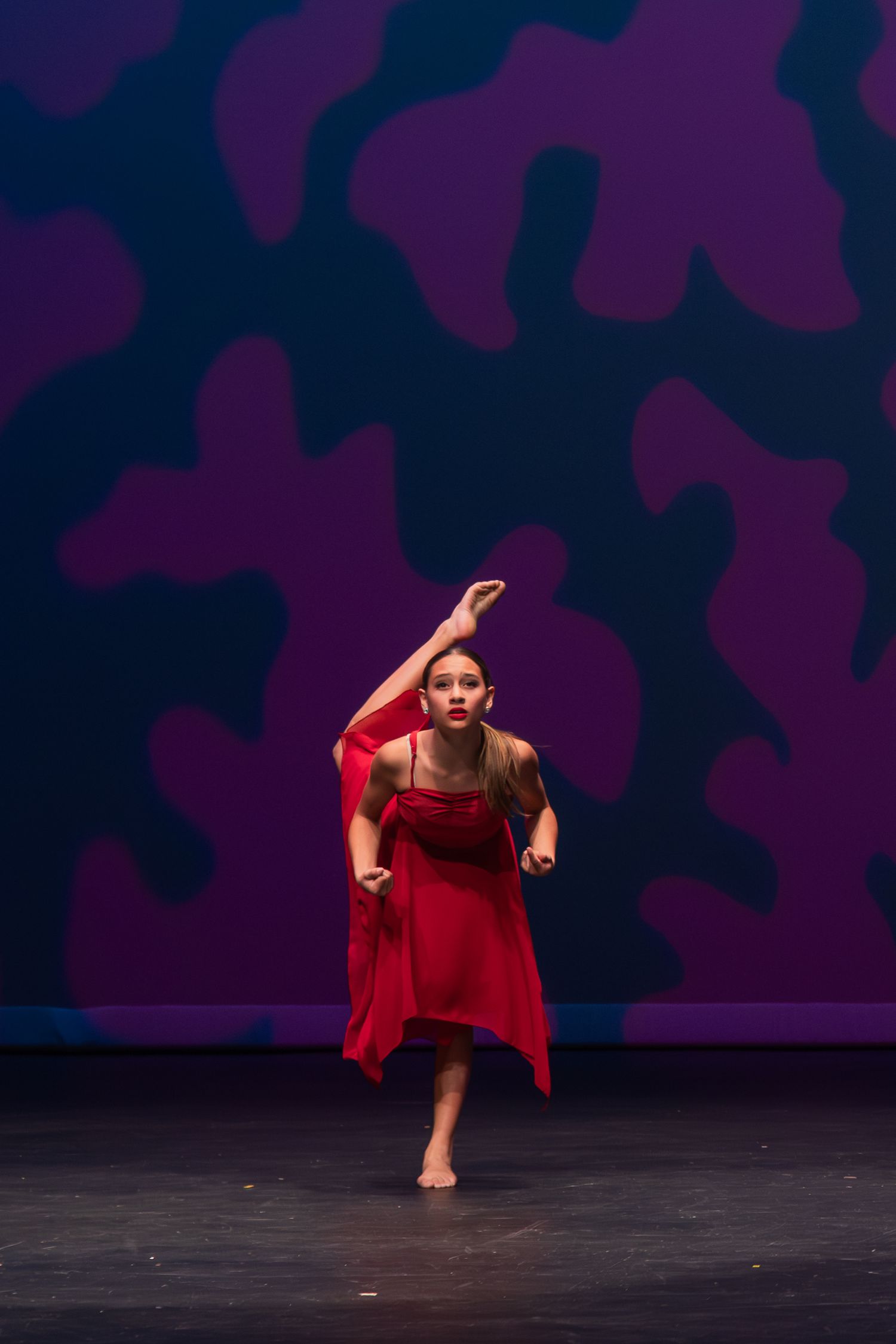 Dancer in flowing red costume performs dramatic contemporary dance movements against dark purple backdrop.