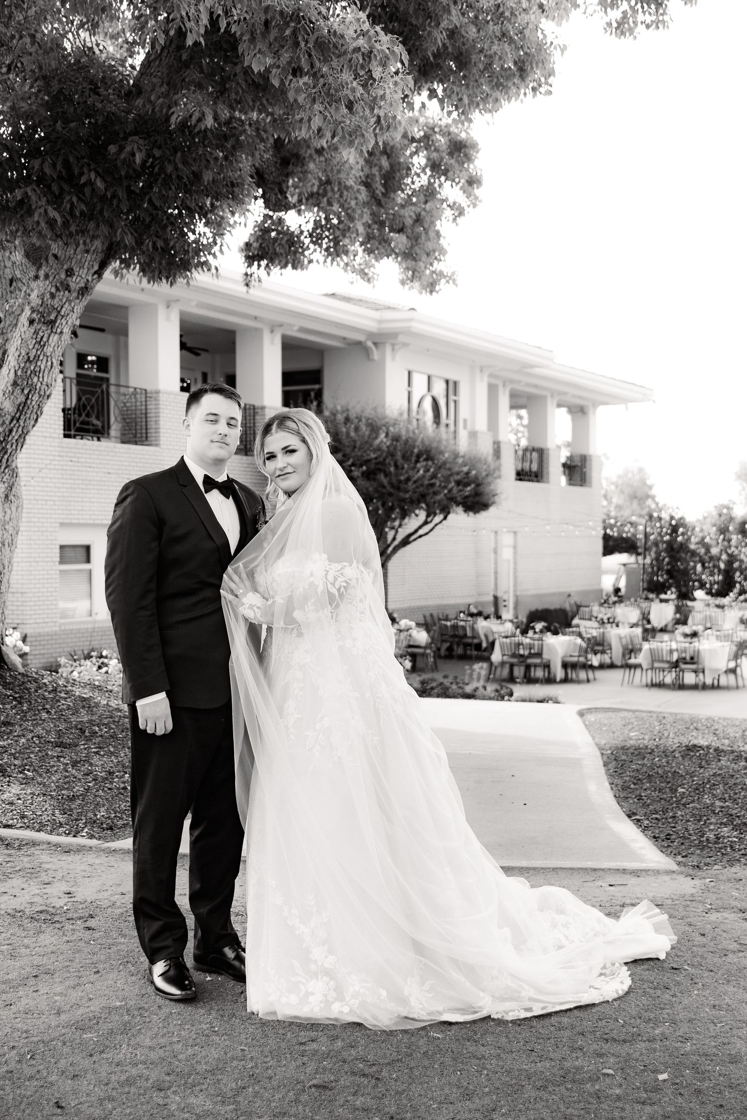 Black and white portrait of a couple in formal wedding attire outside a classic building.