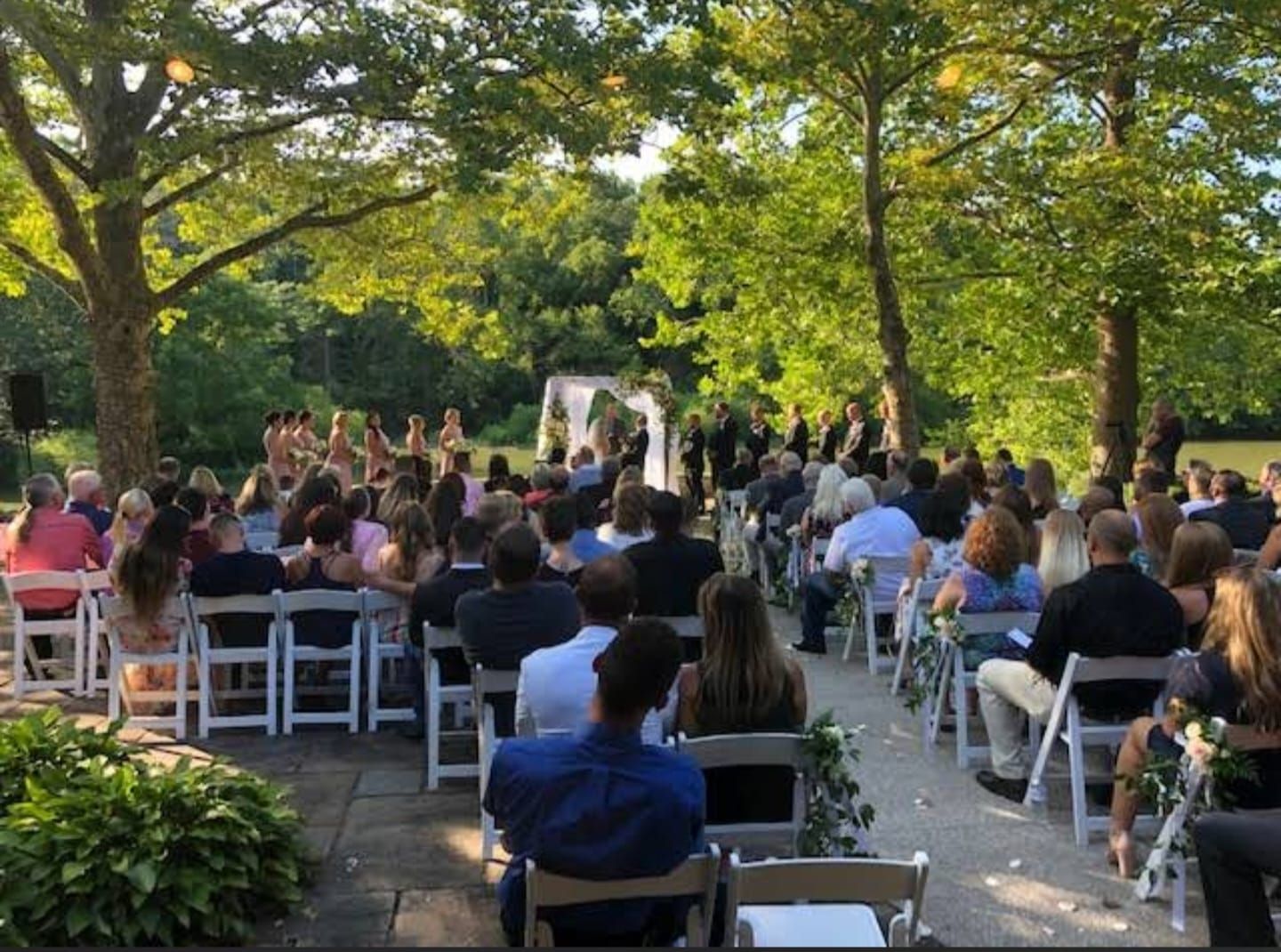 Outdoor wedding ceremony setup with white chairs and natural greenery.