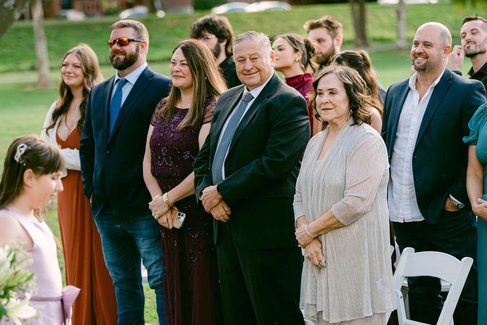 Wedding guests gather outdoors on a sunny day, sharing laughter and conversation during a social celebration.