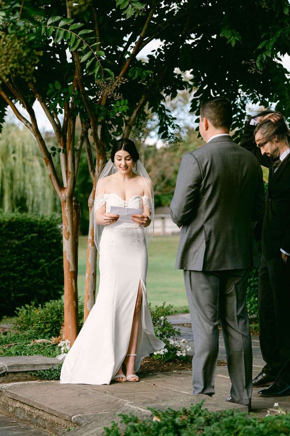A couple shares an intimate moment during their outdoor wedding ceremony under green trees.