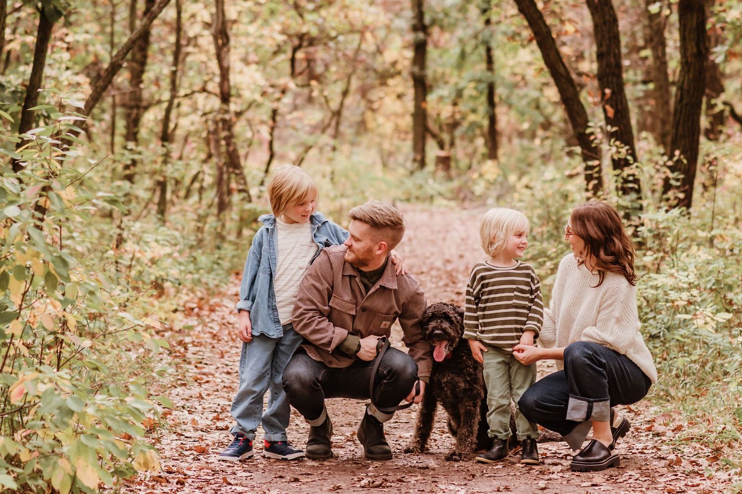 Family sitting together on fallen tree trunk during autumn photo session in wooded forest setting.