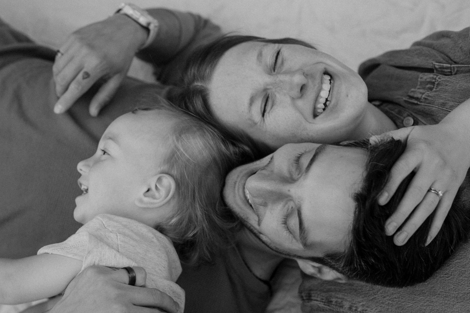 Family of three cuddling on a blanket during their family session, in black and white.