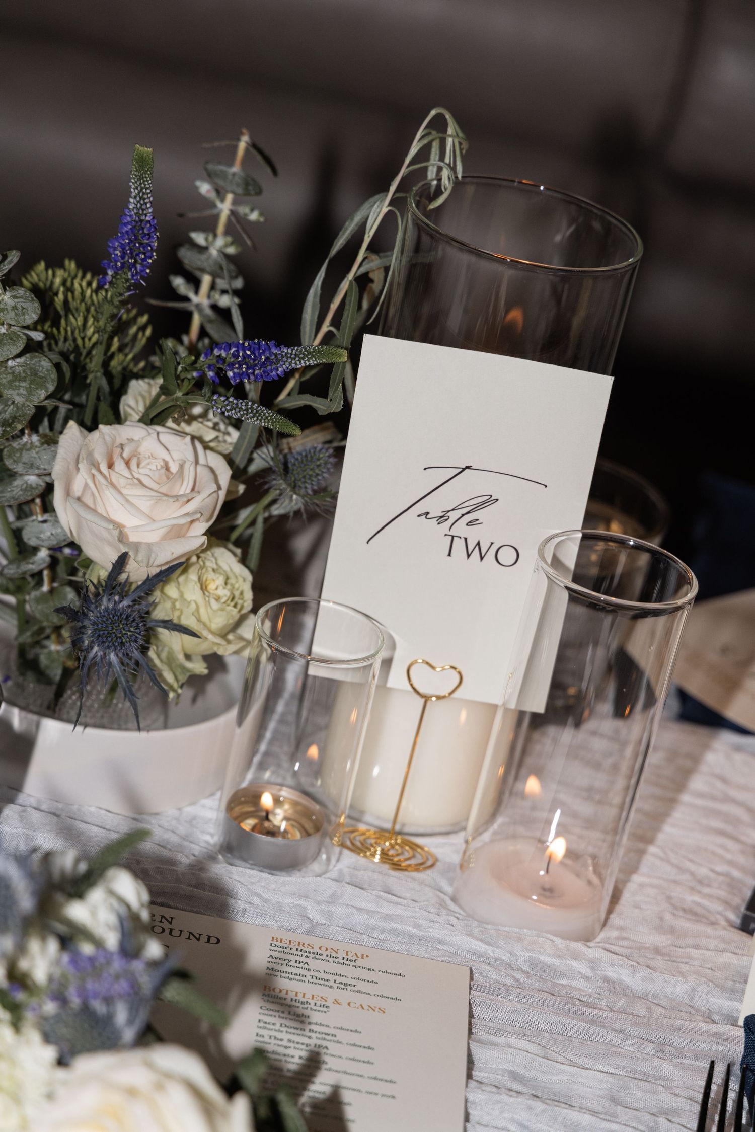 Elegant wedding table decor with white roses, candles, and delicate floral arrangements on a textured tablecloth.