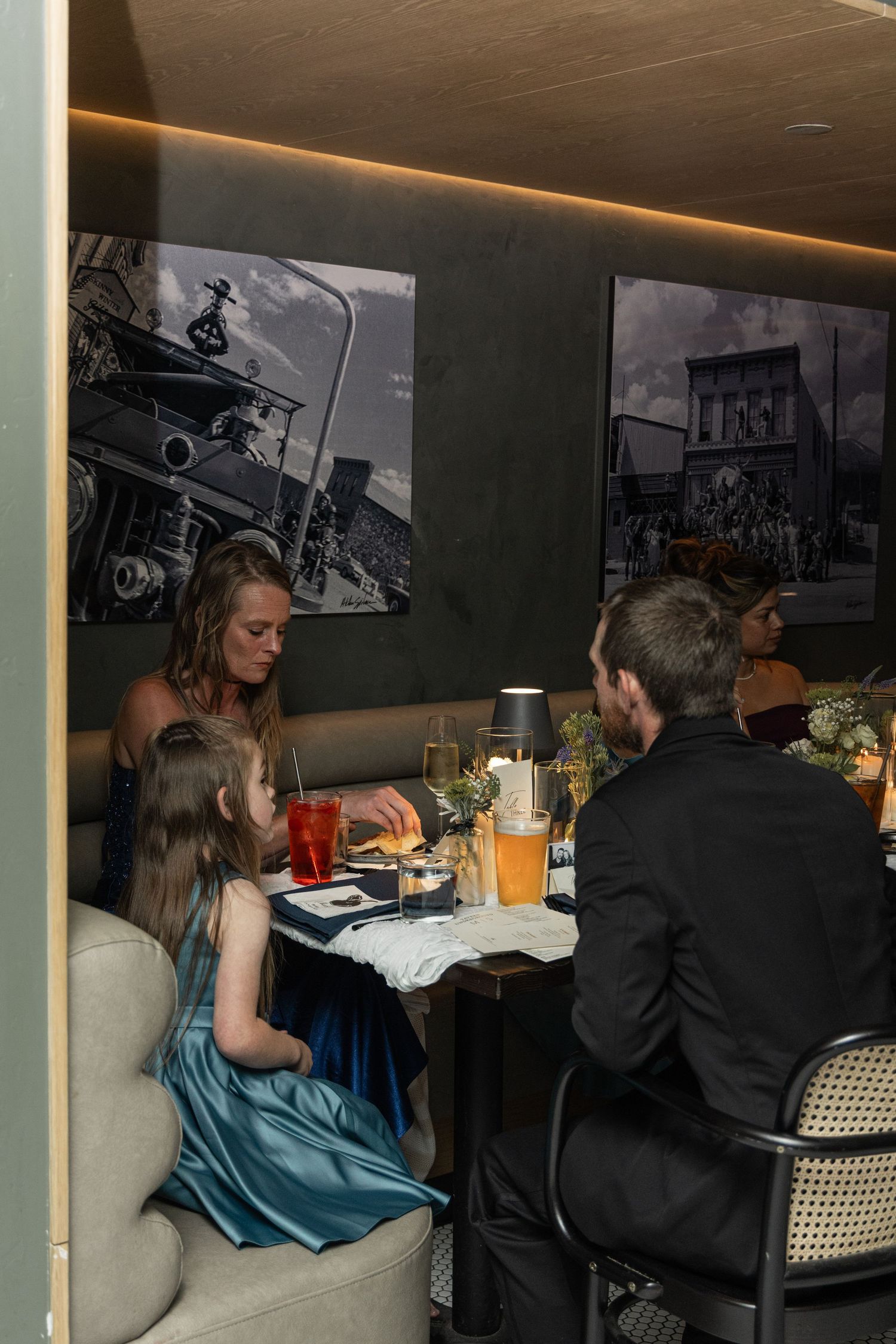 Wedding guests seated at dining tables in a dimly lit restaurant with black and white photos on the wall.