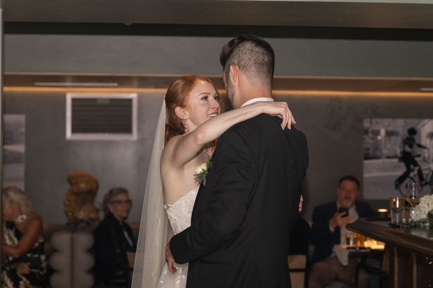 Couples dancing together during a wedding reception in a dimly lit ballroom with atmospheric lighting.