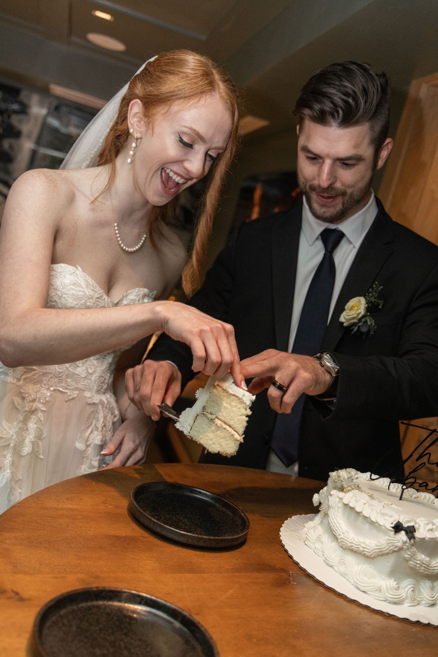 A bride and groom cut their wedding cake together at a wooden table during their reception.