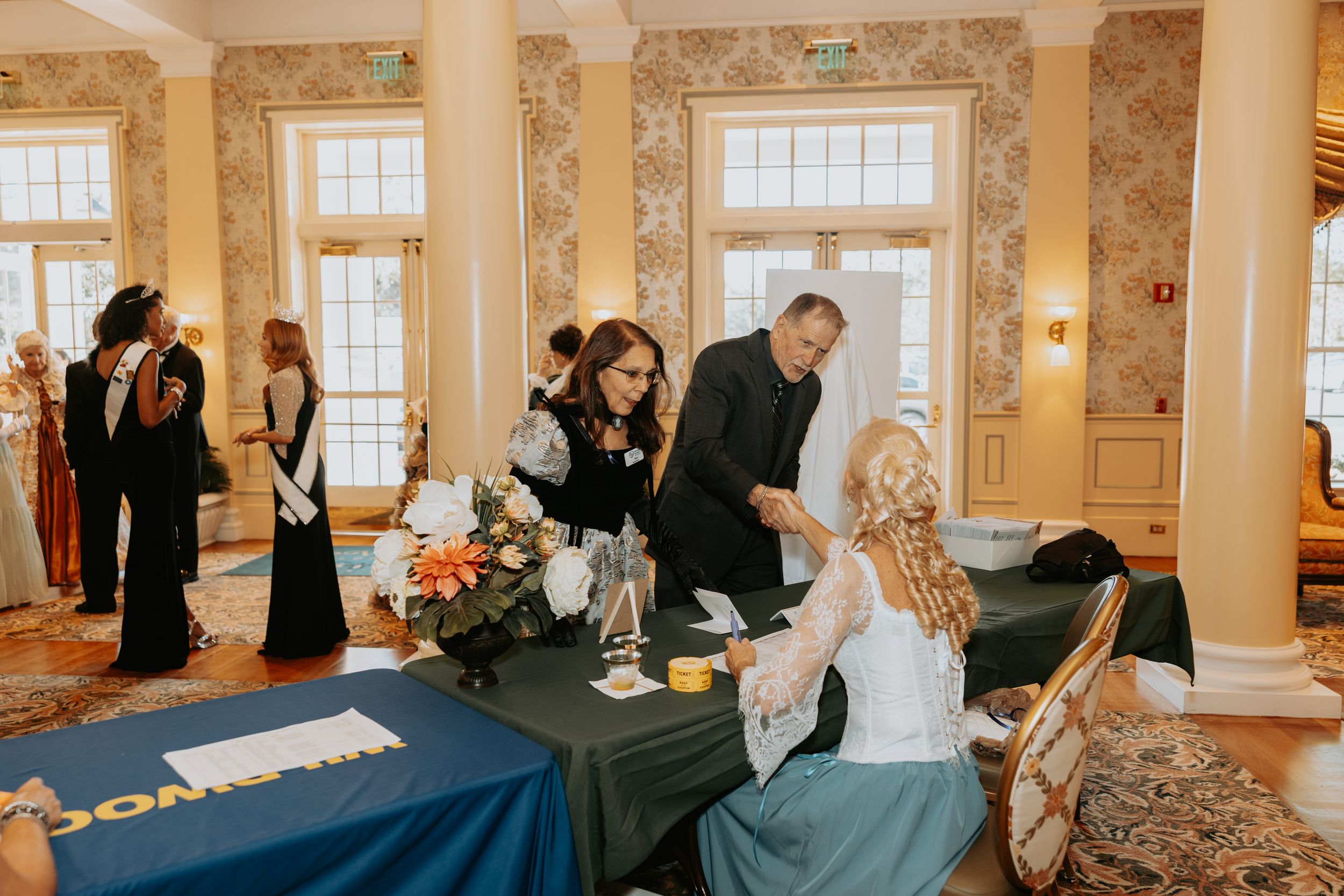 Business professionals raise their hands during an engaging workshop session in a bright, ornate conference room.