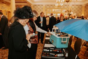 People gather around a blue-covered buffet table at an elegant indoor event with chandeliers.