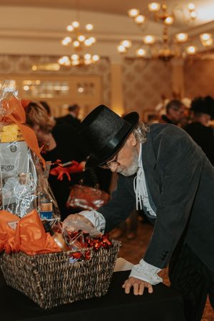 A person in formal attire examines items in a wicker basket at an indoor event.