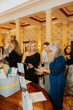 People gathering in an elegant ballroom with pillars examining papers and displays.