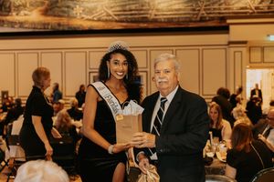 A formal awards ceremony takes place in an elegant ballroom with classical decor.