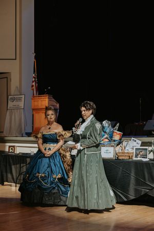 Dancers in period costumes perform an elegant ballroom dance in a historic setting.