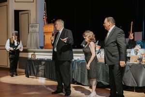 A couple performs an elegant dance routine at a formal event while guests watch from tables in the background.