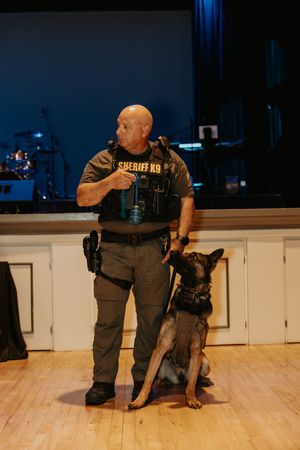 Law enforcement officers in tactical gear conducting a demonstration on wooden floor stage.