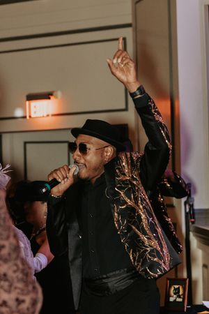Performer in black attire and hat energetically singing on stage.