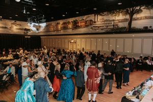 A crowded ballroom filled with people in formal attire mingling at an evening event.
