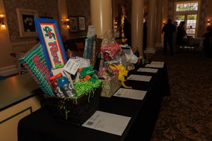 Silent auction display table with colorful gift baskets and bid sheets arranged in an elegant hallway setting.