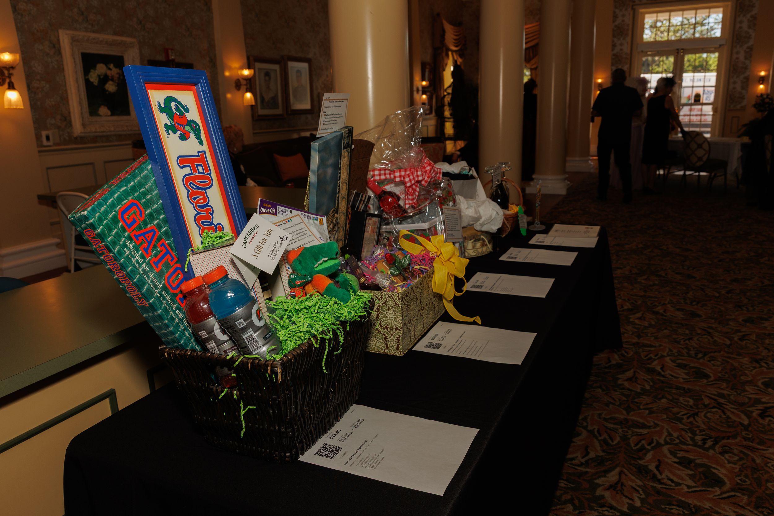 Silent auction display table with colorful gift baskets and bid sheets arranged in an elegant hallway setting.
